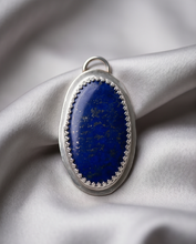 Load image into Gallery viewer, Oval Lapis Lazuli pendant set in handcrafted sterling silver with decorative bezel detailing.
