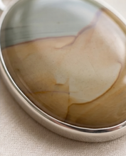 Load image into Gallery viewer, Lifestyle image of handcrafted sterling silver Picture Jasper pendant featuring natural tan, cream, and gray earth-tone patterns